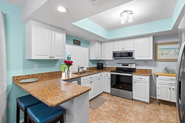 kitchen with stainless steel appliances, white cabinetry, a sink, dark stone countertops, and a peninsula