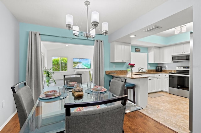 dining space featuring light wood-type flooring, visible vents, a notable chandelier, and baseboards