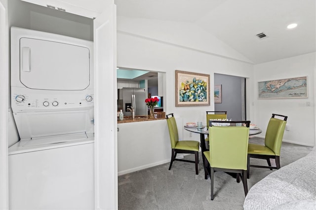 carpeted dining area featuring vaulted ceiling, baseboards, visible vents, and stacked washer / drying machine