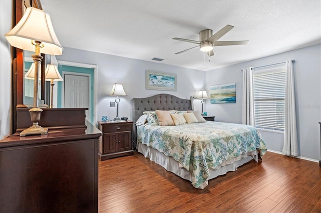 bedroom featuring baseboards, dark wood finished floors, visible vents, and a ceiling fan