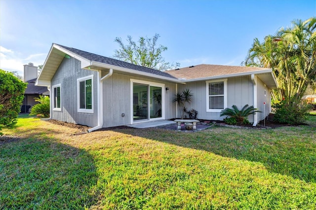 back of property with a shingled roof and a lawn