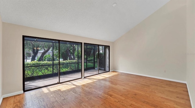 spare room with vaulted ceiling, a textured ceiling, hardwood / wood-style flooring, and baseboards