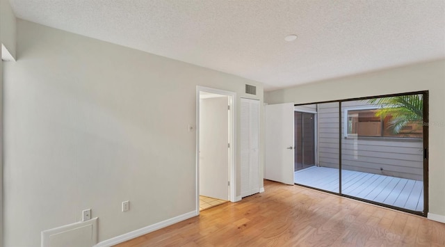 unfurnished bedroom featuring baseboards, a textured ceiling, visible vents, and wood finished floors