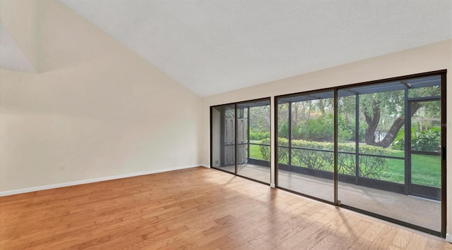 spare room featuring vaulted ceiling, baseboards, wood finished floors, and a healthy amount of sunlight