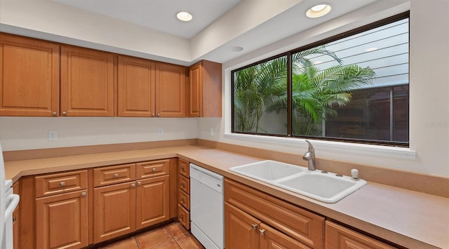 kitchen featuring light tile patterned floors, light countertops, brown cabinetry, white dishwasher, and a sink