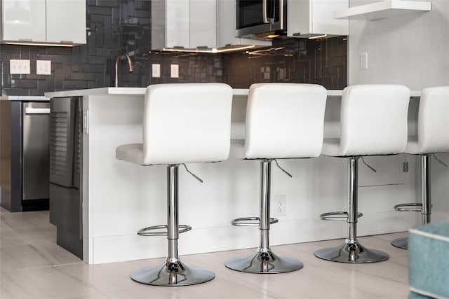 bar with a sink, stainless steel microwave, and backsplash