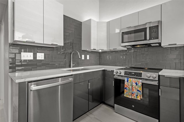 kitchen with modern cabinets, gray cabinetry, appliances with stainless steel finishes, a sink, and light stone countertops