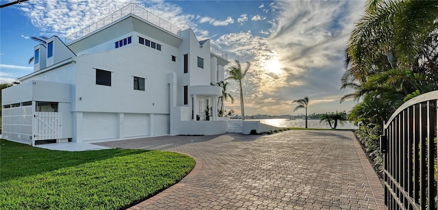 view of side of home featuring a garage, fence, driveway, a lawn, and stucco siding