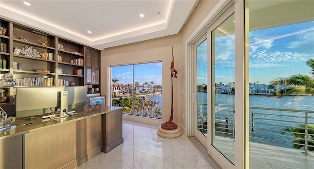 office featuring marble finish floor, a raised ceiling, and a healthy amount of sunlight