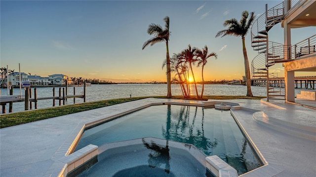 pool at dusk featuring a water view, a pool with connected hot tub, and a boat dock