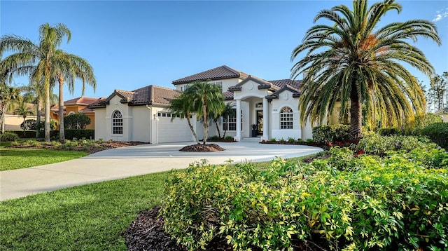 mediterranean / spanish house with a garage, driveway, a tile roof, and stucco siding