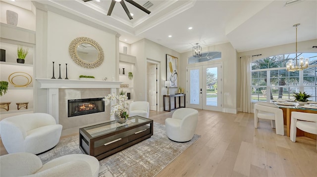 living room featuring built in shelves, a notable chandelier, light wood finished floors, ornamental molding, and a tile fireplace