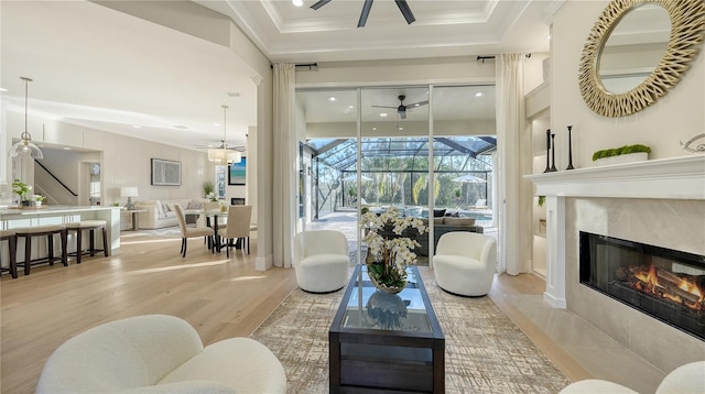 living room with a ceiling fan, a sunroom, a fireplace with flush hearth, light wood-style flooring, and crown molding