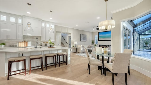 dining area featuring crown molding, light wood-style floors, a glass covered fireplace, a ceiling fan, and stairs