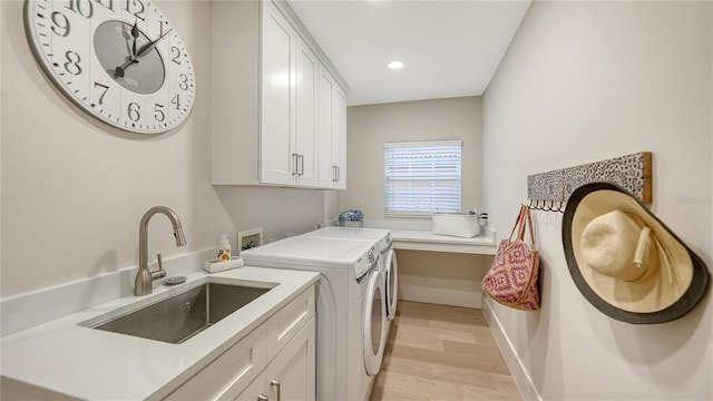 clothes washing area featuring cabinet space, a sink, separate washer and dryer, light wood-type flooring, and baseboards