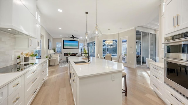 kitchen featuring light wood-style flooring, double oven, open floor plan, a sink, and wall chimney range hood