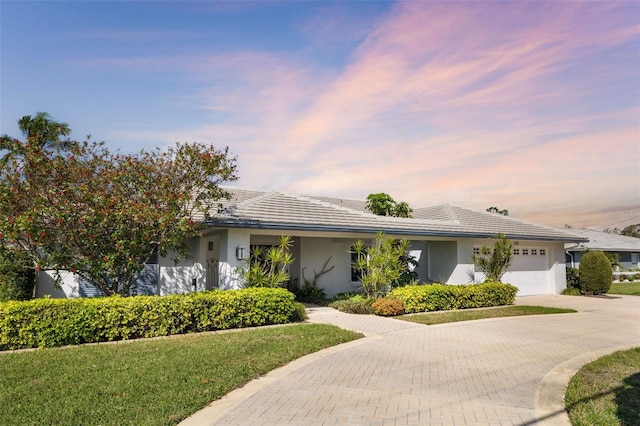 view of front facade with a tile roof, an attached garage, decorative driveway, a yard, and stucco siding