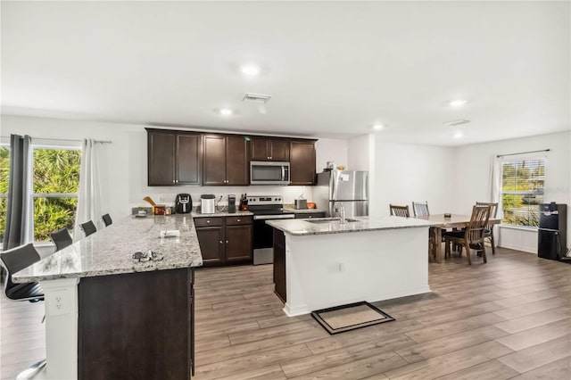 kitchen with a center island with sink, a breakfast bar area, appliances with stainless steel finishes, dark brown cabinets, and light wood-type flooring