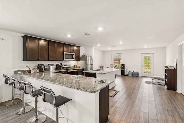 kitchen featuring light wood finished floors, visible vents, appliances with stainless steel finishes, a kitchen breakfast bar, and dark brown cabinets