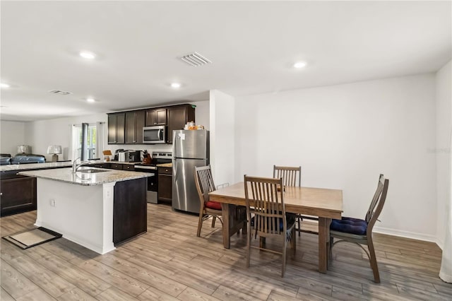 kitchen featuring visible vents, a kitchen island with sink, stainless steel appliances, dark brown cabinets, and light wood-type flooring