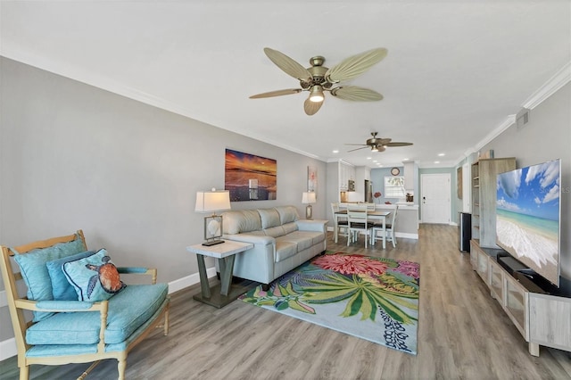 living area featuring visible vents, baseboards, a ceiling fan, light wood-style flooring, and crown molding