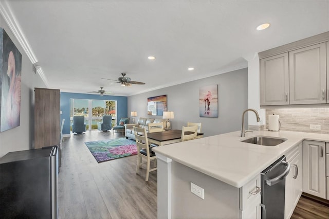 kitchen featuring a peninsula, a sink, open floor plan, ornamental molding, and dishwasher