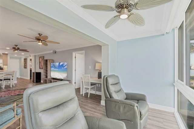 living area with ornamental molding, light wood-type flooring, a ceiling fan, and baseboards