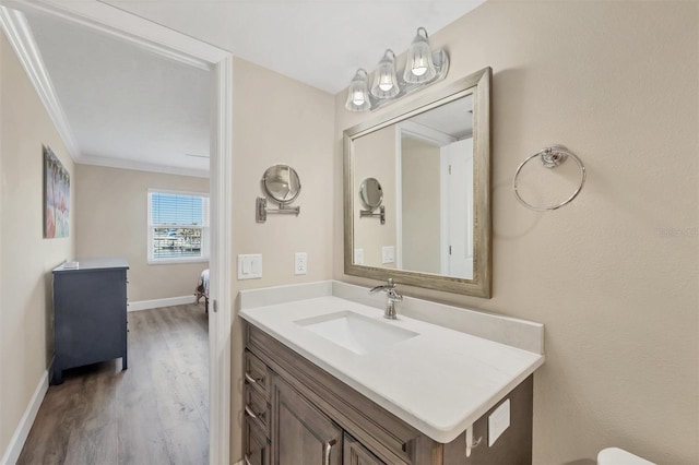 ensuite bathroom with ensuite bathroom, wood finished floors, vanity, baseboards, and ornamental molding