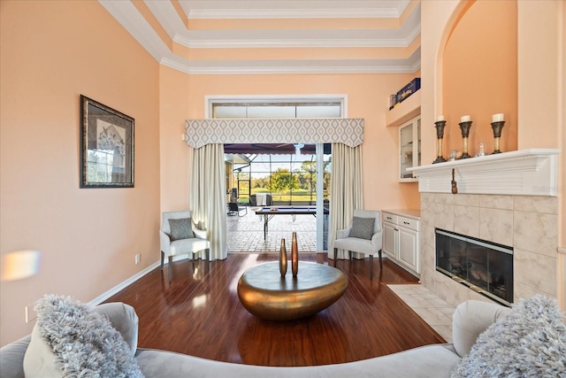 living area with baseboards, a tile fireplace, a towering ceiling, ornamental molding, and wood finished floors