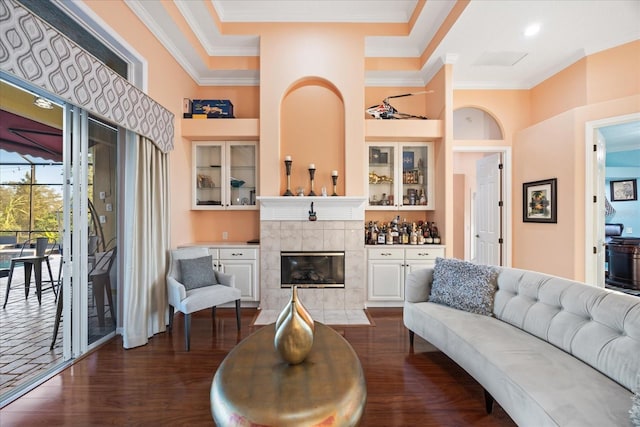 living room with a towering ceiling, dark wood-style floors, a fireplace, and ornamental molding