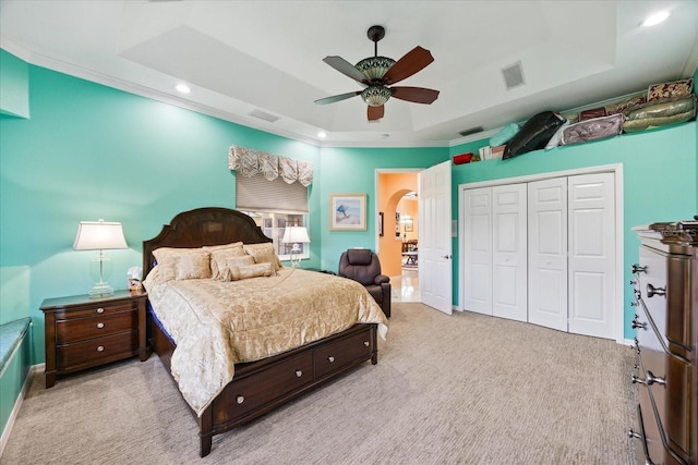 carpeted bedroom featuring a tray ceiling, a closet, visible vents, and arched walkways