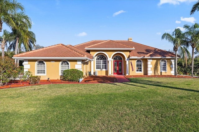 mediterranean / spanish house with a chimney, a front yard, a tile roof, and stucco siding