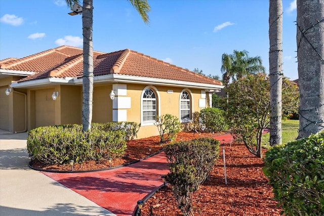 view of front of home featuring a tiled roof, concrete driveway, an attached garage, and stucco siding