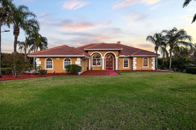 mediterranean / spanish-style home featuring stucco siding, a chimney, a front lawn, and a tiled roof