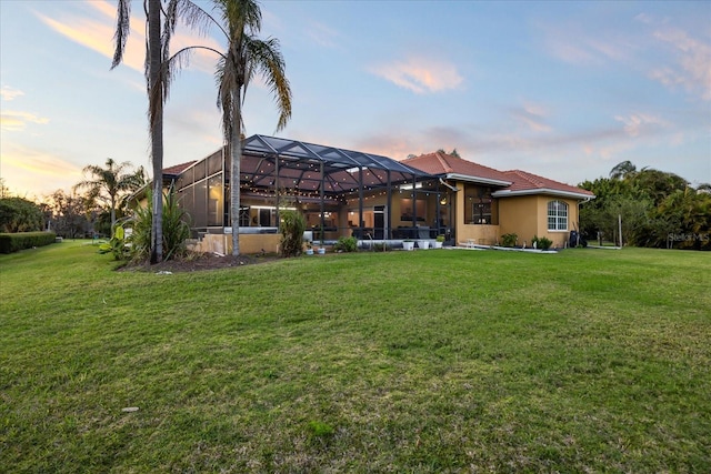 back of property featuring glass enclosure, a lawn, and stucco siding