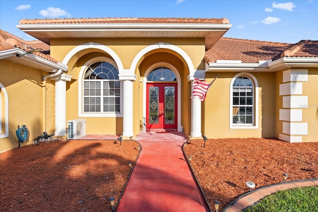 view of exterior entry with stucco siding, a tile roof, ac unit, and french doors