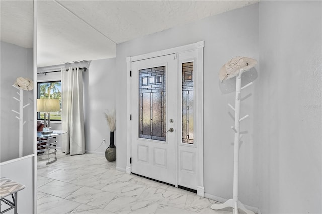 foyer featuring marble finish floor, baseboards, and a textured ceiling