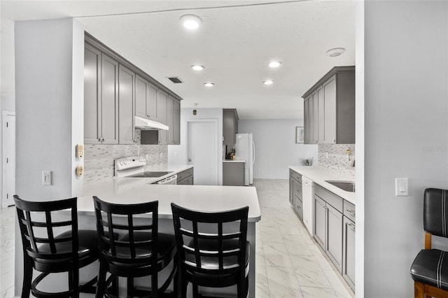 kitchen with marble finish floor, gray cabinetry, white appliances, a peninsula, and under cabinet range hood