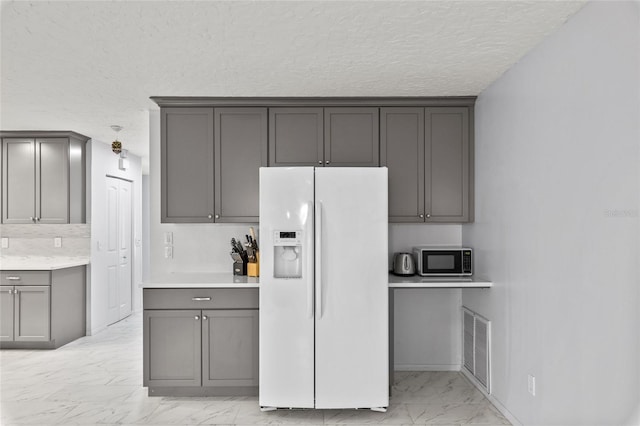 kitchen with white refrigerator with ice dispenser, visible vents, marble finish floor, gray cabinets, and light countertops