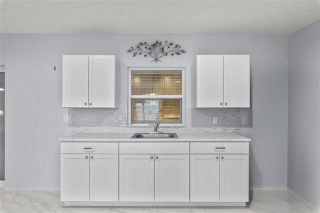 kitchen featuring a sink, white cabinetry, baseboards, marble finish floor, and tasteful backsplash