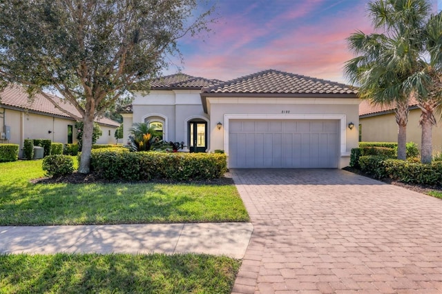 mediterranean / spanish home featuring an attached garage, a tile roof, decorative driveway, and stucco siding