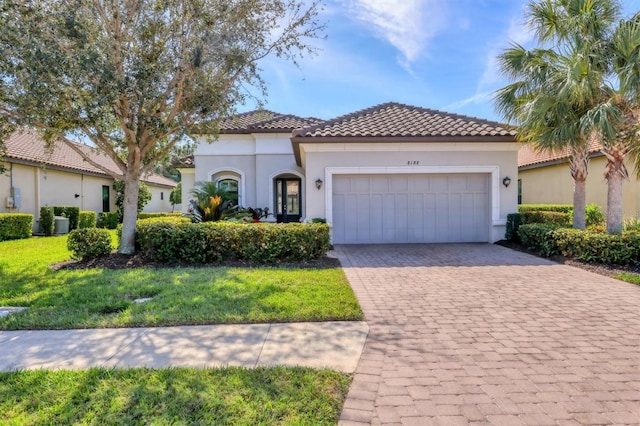 mediterranean / spanish home featuring decorative driveway, a tile roof, stucco siding, an attached garage, and a front lawn