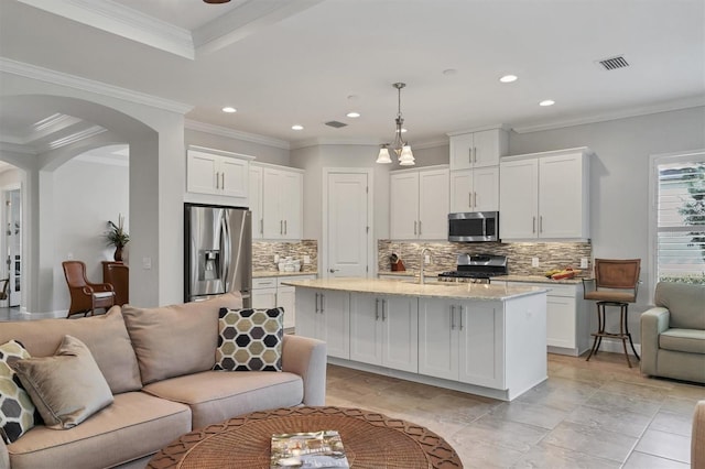 kitchen with arched walkways, hanging light fixtures, appliances with stainless steel finishes, open floor plan, and a kitchen island with sink