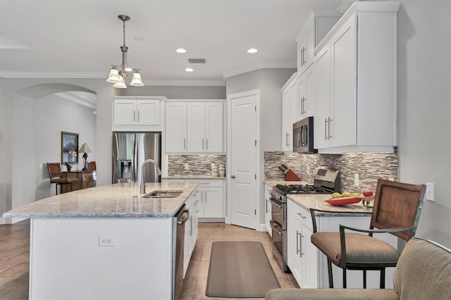 kitchen featuring a kitchen island with sink, a sink, white cabinets, hanging light fixtures, and appliances with stainless steel finishes