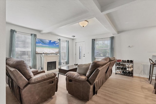 living area featuring light wood finished floors, visible vents, beam ceiling, and a glass covered fireplace