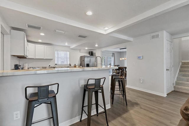 kitchen with stainless steel refrigerator with ice dispenser, visible vents, wood finished floors, a peninsula, and a kitchen bar