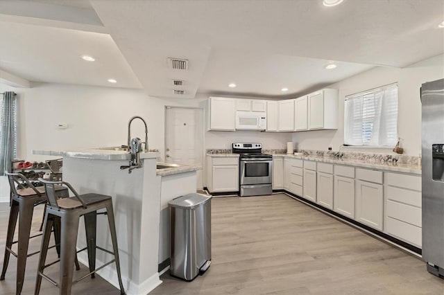 kitchen featuring light wood finished floors, a breakfast bar area, stainless steel appliances, visible vents, and white cabinets