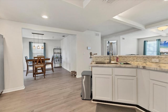 kitchen featuring light wood finished floors, light countertops, hanging light fixtures, white cabinets, and a sink