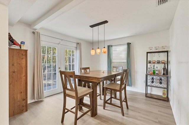 dining room featuring french doors, light wood finished floors, beamed ceiling, and visible vents