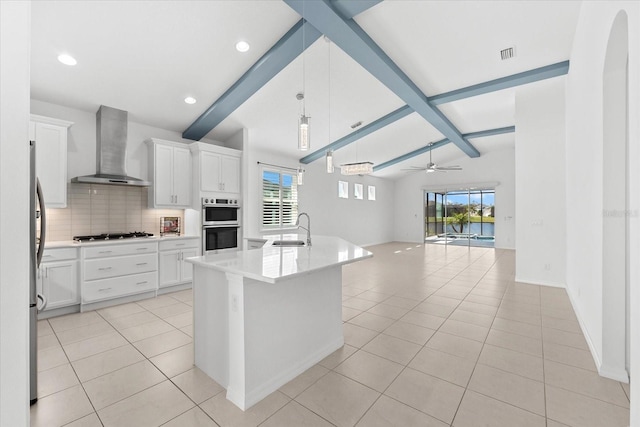 kitchen with a center island with sink, white cabinets, open floor plan, wall chimney range hood, and a sink